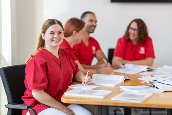 Auszubildende zur Pflegefachfrau sitzt am Tisch mit Unterlagen und lächelt – motivierte Lernsituation beim Caritasverband Westeifel.