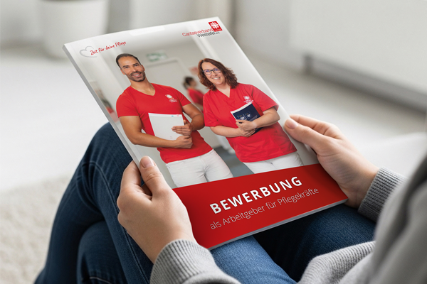 Zwei Hände halten eine Bewerbungsbroschüre der Caritas mit Informationen zu Berufen als Pflegefachkraft und Pflegehelfer.