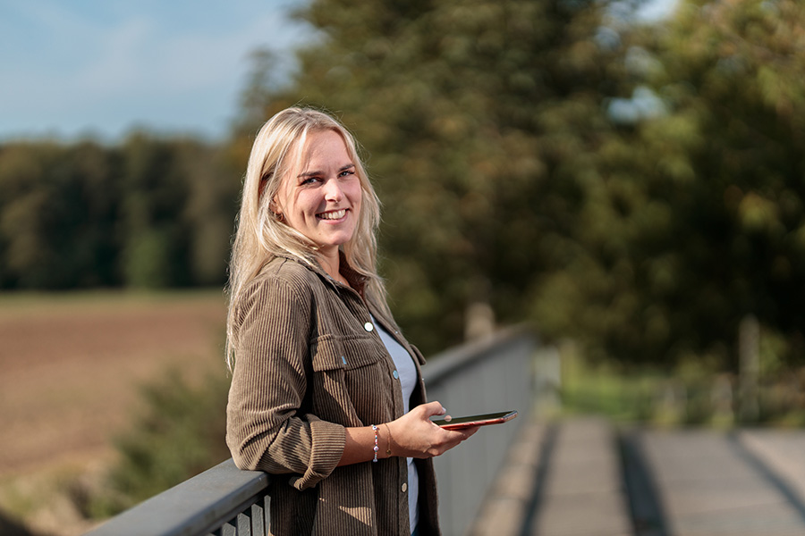 Sozialarbeiterin steht mit Smartphone, lächelt in die Kamera – große Flexibilität und Work-Life-Balance beim Caritasverband Westeifel.