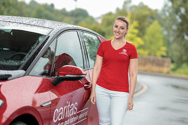 Pflegefachfrau steht am Auto und lächelt – symbolisch für freundliche Arbeitsatmosphäre in der ambulanten Pflege.