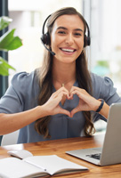 Verwaltungsangestellte lächelt in die Kamera, sitzt am Schreibtisch und formt ein Herz mit den Händen.