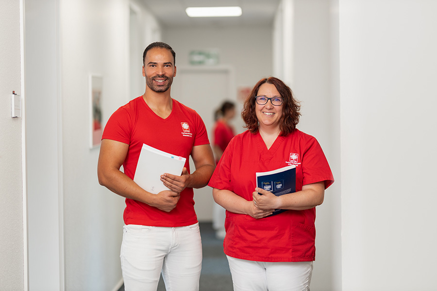 Azubi Pflegefachmann steht mit Praxisanleiterin und lächelt in die Kamera - 1:1 Betreuung in der Ausbildung beim Caritasverband Westeifel.